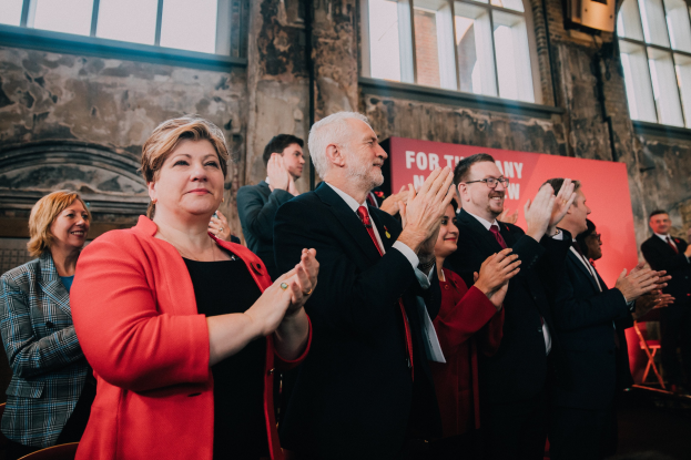 Eine Gruppe von Menschen, die vor einer Menge jubeln, mit einem Banner im Hintergrund, das einen Wahlsieg anzeigt.