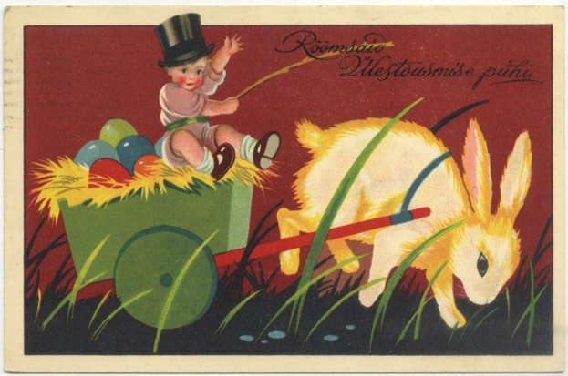 Eine alte Postkarte zeigt ein Baby in einem Zylinder, das einen mit bunten Ostereiern gefüllten Karren schiebt, begleitet von einem Hasen, mit handgeschriebenen Ostergrüßen.
