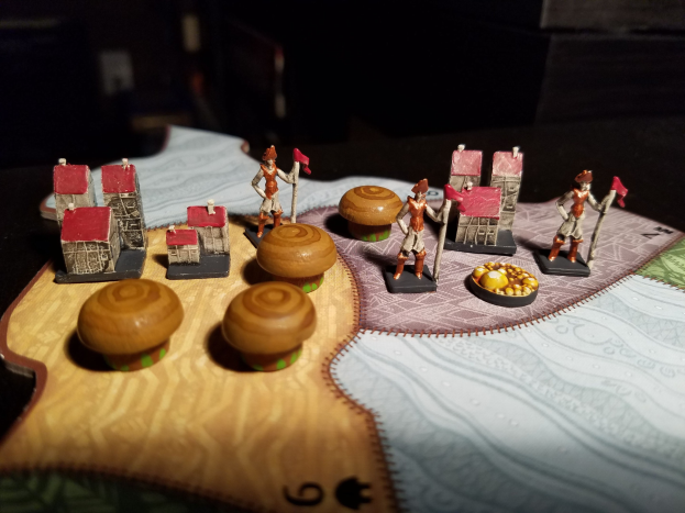 Nahaufnahme eines Spielbretts mit Miniaturen, einschließlich Spielzeug, Gebäuden und anderen Gegenständen auf einem dunklen Hintergrund.