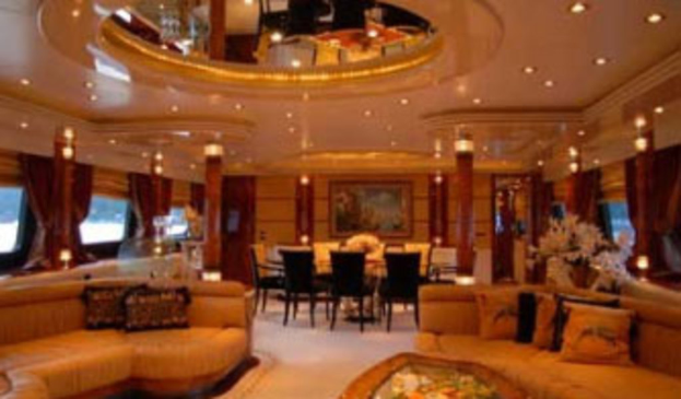 Ein Hotellobby mit Sofas, Stühlen, Tischen, Blumenarrangements im Vordergrund, Fenstern mit Vorhängen und Lampen auf beiden Seiten, einem gerahmten Kunstwerk und Deckenleuchten im Hintergrund sowie einem großen Spiegel oben.