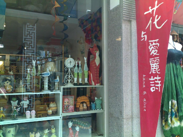 Eine Ausstellung mit verschiedenen Gegenständen, darunter ein Banner, eine Schaufensterpuppe und ein Traumfänger auf der linken Seite und ein Glasfenster, das Spielzeug, eine Uhr und einen Schrank auf der rechten Seite zeigt.