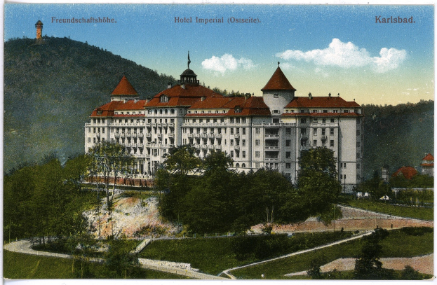 Alte Ansichtskarte des Hotels Imperial in Karlsbad, Deutschland, mit einem großen Gebäude mit Fenstern, umgeben von Bäumen, Pflanzen, Gras, einem Pfad, einer Baumgruppe, Hügeln und einem bewölkten Himmel, mit Text oben.
