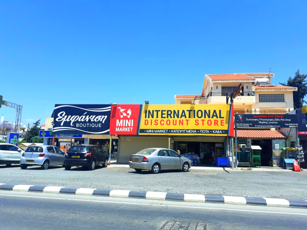 Internationaler Discount-Laden an einer Straßenecke mit umliegenden Gebäuden, Fahrzeugen, Verkehrsinfrastruktur und wolkenlosem Himmel.