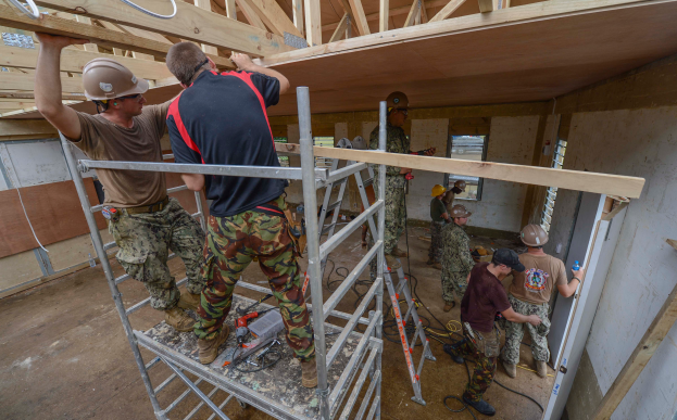Eine Gruppe von Bauarbeitern in Helmen steht auf Leitern und arbeitet an einem Gebäude unter construction mit Werkzeugen und Materialien, die herumliegen, mit einer Wand und einem Fenster im Hintergrund.