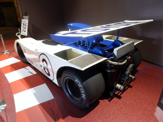 Ein weißer und blauer Rennauto in einer Museumsausstellung auf dem Goodwood Festival of Speed, umgeben von Barrieren und Informationsschildern.