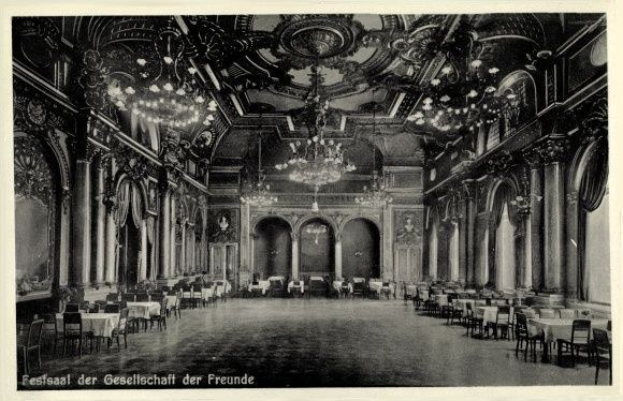 Schwarzes und weißes Foto eines großen Raumes mit Tischen, Stühlen, Säulen, Bögen und Deckenleuchter, beschriftet mit "Festival der Gesellschaft der Freunde, Berlin" unten.