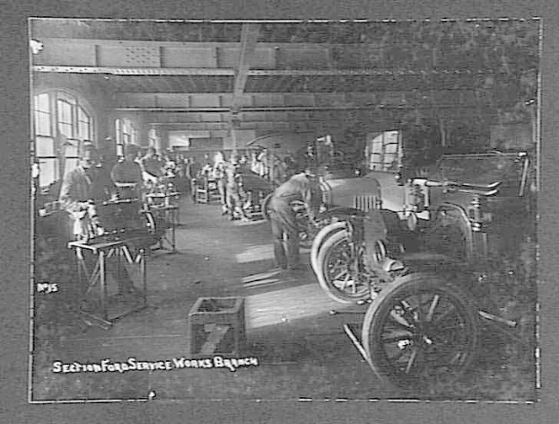 Schwarzes und weißes Foto von Männern, die an Autos in einer Ford-Werkstatt arbeiten, mit Fahrzeugen, Werkzeugen und Fenstern im Bild.