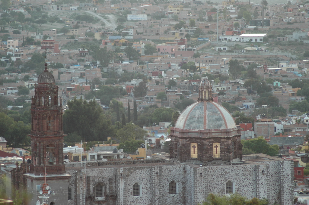 Eine Luftaufnahme einer Stadt mit einer Kirche im Vordergrund, die Bäume, Gebäude, Straßen und Masten zeigt.