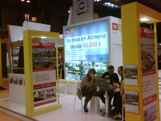 Eine Gruppe von Menschen sitzt in Stühlen um einen Tisch, schaut auf einen Laptop und hat mehrere Flyer mit verschiedenen Werbeanzeigen daneben.