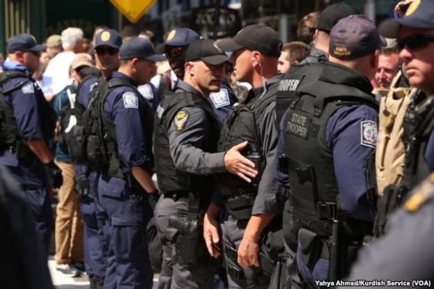 Eine Gruppe von Polizisten in Uniform, die zusammen auf einer Straße stehen, einige mit Waffen, mit Gebäuden und Schildern im Hintergrund.