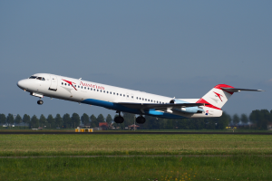 Ein Embraer ERJ-190-Flugzeug der Austrian Airlines beim Start am Frankfurter Flughafen, mit grünem Gras, Bäumen und Gebäuden im Hintergrund und dem Himmel darüber.