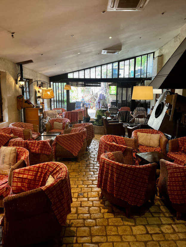 Ein geräumiger Eingangsbereich mit Stühlen, Tischen, Sofas mit Kissen, Wandlampen, einer Deckenklimaanlage und großen Glasfenstern an der Rückseite.