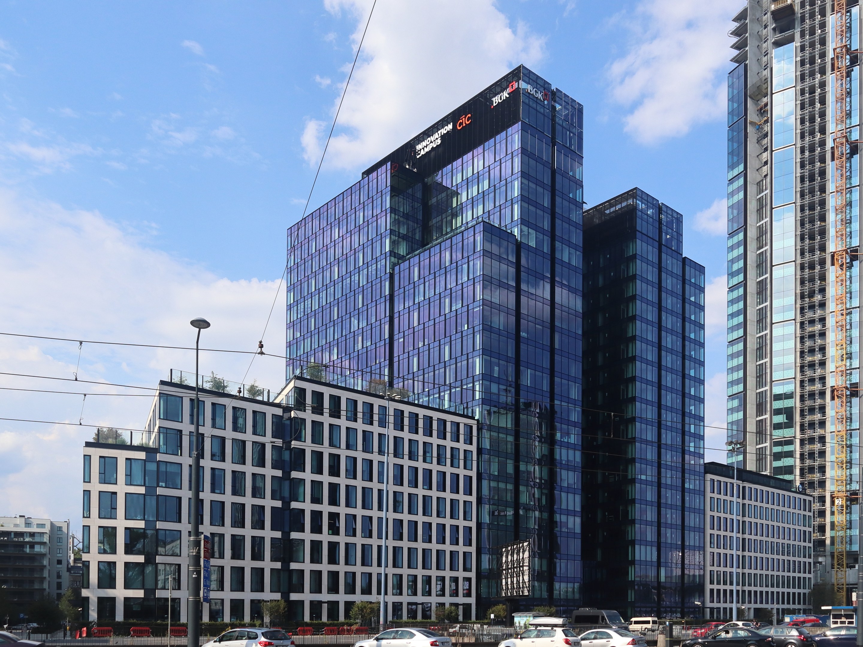 Zentrale der Deutschen Bank in Frankfurt, Deutschland, ein großes Gebäude mit vielen Fenstern, umgeben von Straßeninfrastruktur, Fahrzeugen, Grünflächen und einem bewölkten Himmel.