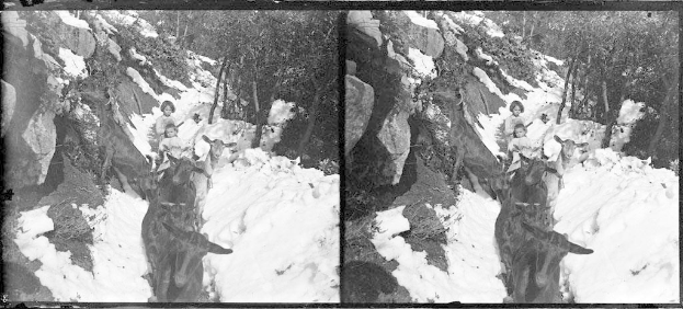 Schwarzes und weißes Foto von Menschen in Winterkleidung, die Rentiergeweihte durch unberührten Schnee reiten, mit Bäumen und Felsen im Hintergrund.