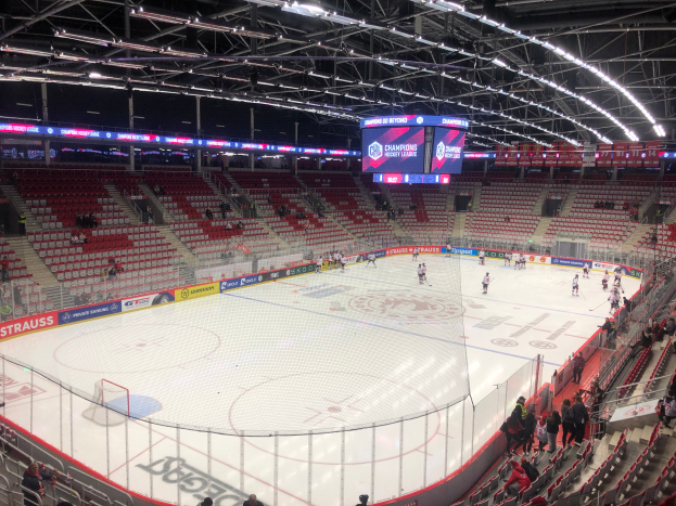 Ein Eishockeyspiel in einer großen Arena mit Zuschauern, einem Zaun um die Eisfläche, einem Bildschirm mit der Aufschrift "St. Louis Blues vs Detroit Red Wings", Metallrahmen und einer Decke mit Deckenleuchten.