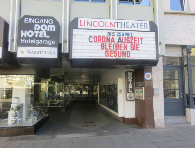 Außenansicht des Lincoln Theaters in Berlin, Deutschland, mit Glasfenstern und -türen sowie einer Schautafel und einem Blick ins Innere auf eine städtische Szenerie.