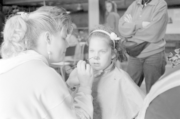 Ein Make-up-Artist trägt Make-up auf das Gesicht eines jungen Mädchens auf, während der Hintergrund unscharf ist.