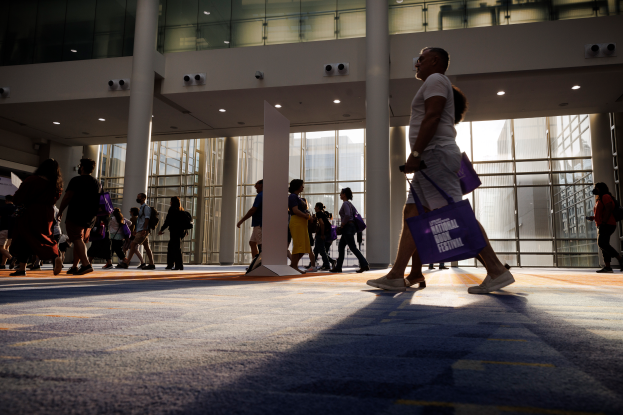 Eine Gruppe von Menschen geht durch ein geräumiges Gebäude mit Glaswänden, Säulen und Deckenleuchten, einige tragen Taschen, wahrscheinlich besuchen sie die National Book Festival.