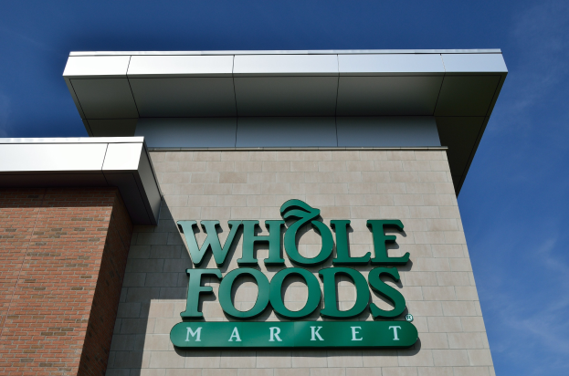 Außensicht eines Whole Foods Market-Gebäudes mit seiner Beschriftung und einem hellblauen Himmel im Hintergrund.