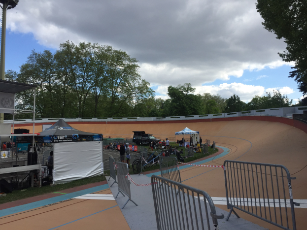 Gruppe von Radfahrern auf einer Schotterstrecke bei den UCI BMX-Weltmeisterschaften 2018, mit Zelten, Fahrzeugen und Bäumen im Hintergrund.