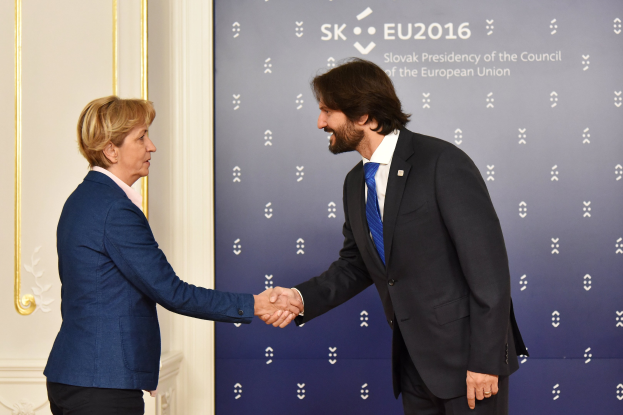 Bundeskanzlerin Angela Merkel und Bundespräsident Joachim Gauck geben sich die Hand vor einer Wand mit einem "EU-Gipfel"-Banner und einer Tür im Hintergrund, beide lächeln.