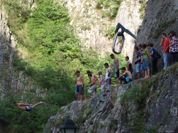 Menschen auf einem Hügel auf der rechten Seite, ein Mann springt nach links, mit Bäumen und Hügeln im Hintergrund.