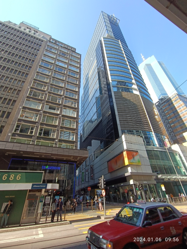 Ein rotes Auto fährt auf einer von hohen Wolkenkratzern gesäumten Stadtstraße, mit Passanten, Verkehrsampeln und verschiedenen Schildern.