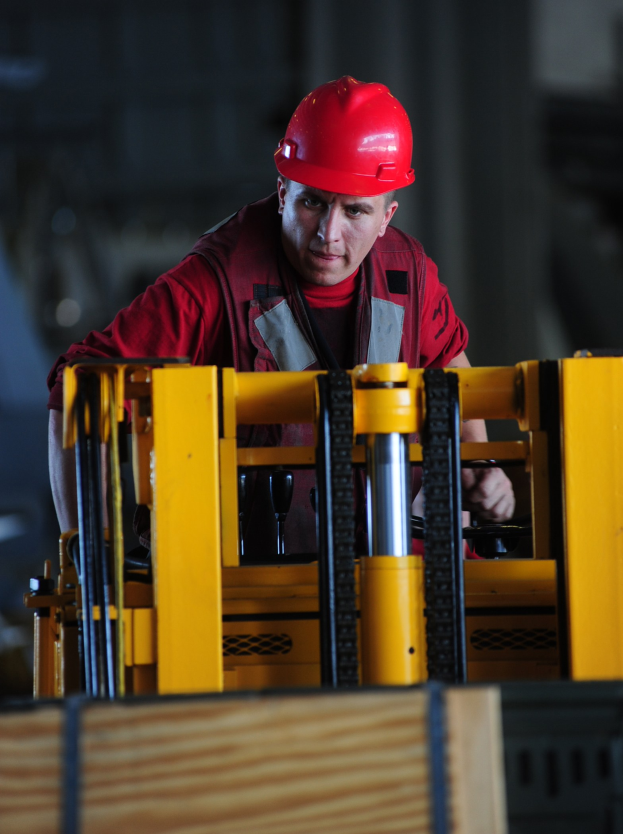 Mann in rotem Helm und rotem Kleid, der einen Gabelstapler bedient.