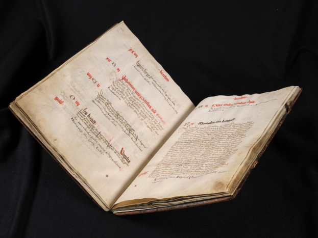 Ein offenes Buch mit rotem Text auf weißen Seiten, vor schwarzem Hintergrund, das wie eine Bibel aussieht.