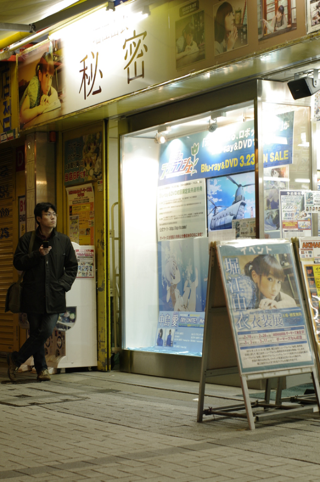 Ein Mann steht mit einem Handy in der Hand und trägt eine Tasche, während Schilder mit Text, Geschäfte, Lichter und Papiere mit Text im Hintergrund zu sehen sind.