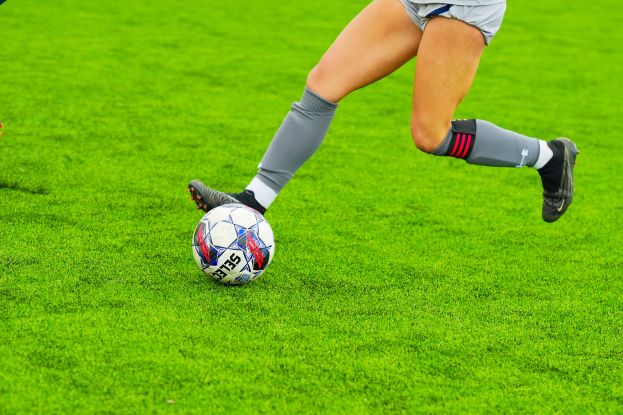 Eine Frau in einem Sportoutfit kickt einen Fußball auf einem saftig grünen Feld.