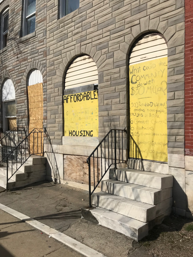 Verschlossenes Gebäude mit "Bezahlbares Wohnen"-Schild, Treppe mit Geländer und Straße unten.