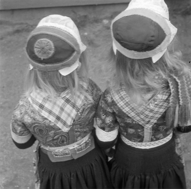 Zwei junge Mädchen in traditionellen bayrischen Kleidern und Hüten stehen Seite an Seite vor einer Wand in einem Schwarz-Weiß-Foto.