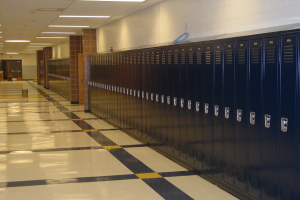 Eine lange Reihe von Spinden in einem Schulflur mit einem gefliesten Boden, einer Wand im Hintergrund, Deckenleuchten und ein paar verstreuten Gegenständen.