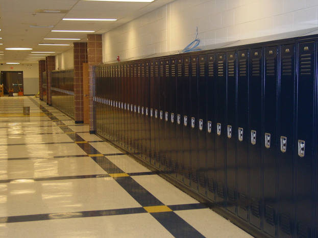 Eine lange Reihe von Spinden in einem Schulflur mit einem gefliesten Boden, einer Wand im Hintergrund, Deckenleuchten und ein paar verstreuten Gegenständen.