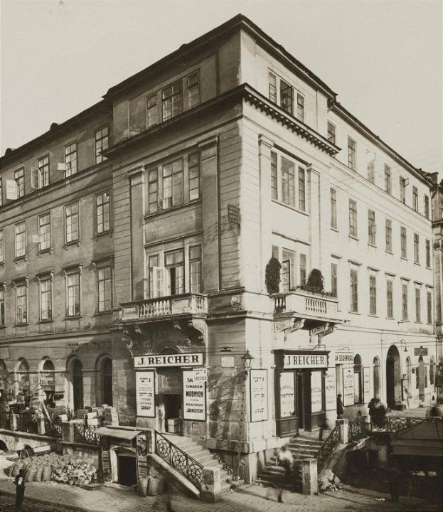 Das J Reicher Hotel in Berlin, ein altes Gebäude mit Fenstern, Treppen mit Geländern, Schildern und Blumentöpfen sowie einigen Menschen und dem Himmel im Hintergrund.