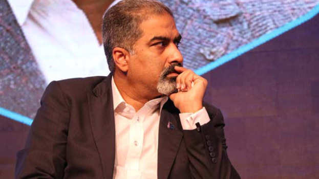 Ein Mann im Anzug und Krawatte sitzt auf einer Bühne und sieht konzentriert auf einen Bildschirm.