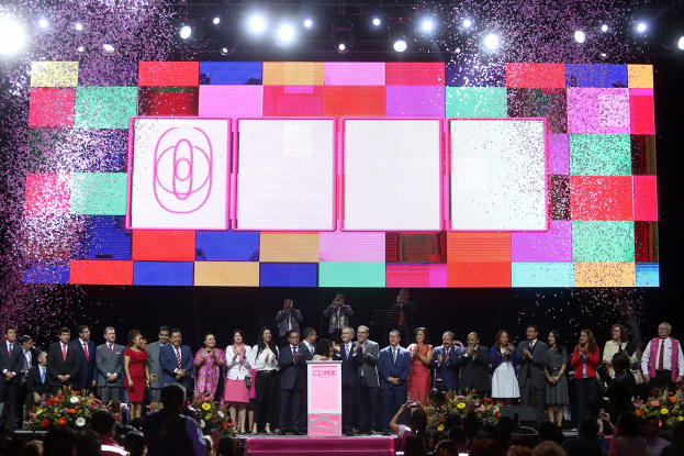 Eine Gruppe von Menschen steht auf einer Bühne mit einem Podium, Blumengestecken auf beiden Seiten und einem großen Bildschirm im Hintergrund während der Eröffnungszeremonie des 2018 China International Film Festival.