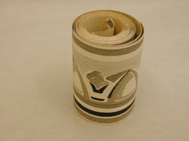 Ein zylindrischer hellbrauner Karton-Toilettenpapier-Roll mit leichten Knittern steht auf einem glatten hellholzbefarbenen Tisch.