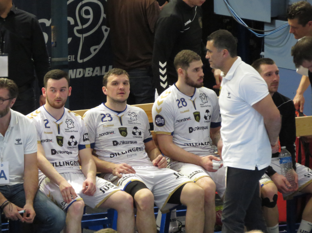 Eine Gruppe von Männern sitzt auf einer Bank, einige halten Flaschen, im Hintergrund eine Fahne mit der Aufschrift "Nordkraque vs Bordeaux."