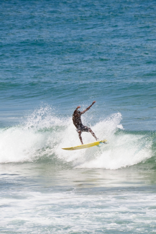 Mann steht auf einem Surfbrett und reitet eine Welle.