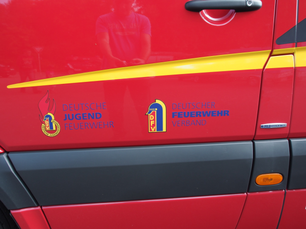 Roter Van mit einer gelben Streifen, Türgriff, Schildlogo mit einem Löwen in einem Lorbeerkranz und der Inschrift "Deutscher Jugendfeuerwehrverband".