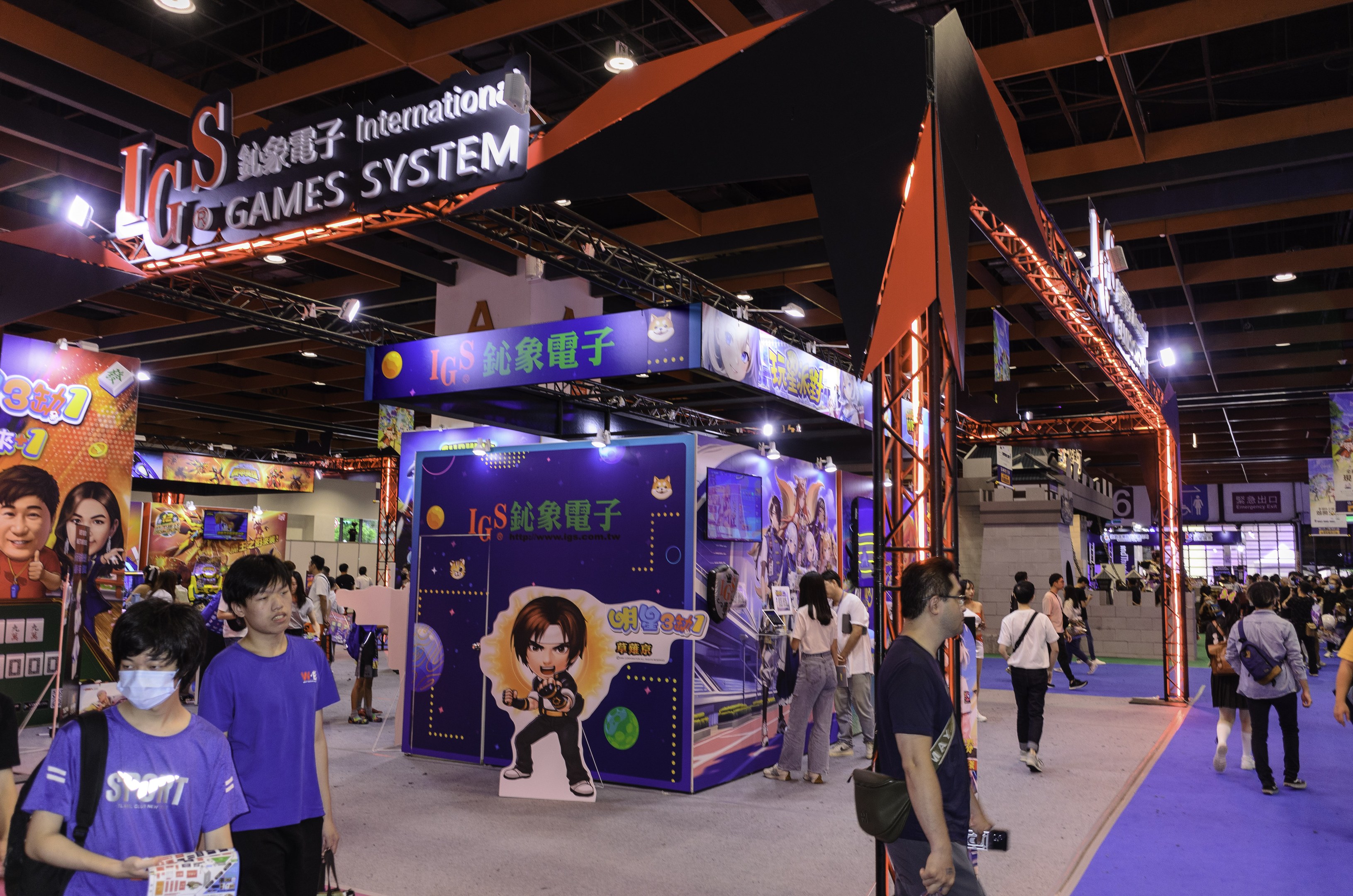 Menschen gehen durch einen Convention Hall auf einer Gaming-Messe in China, einige tragen Taschen und halten Gegenstände, mit Display-Boards, Deckenbeleuchtung und Teppichboden.