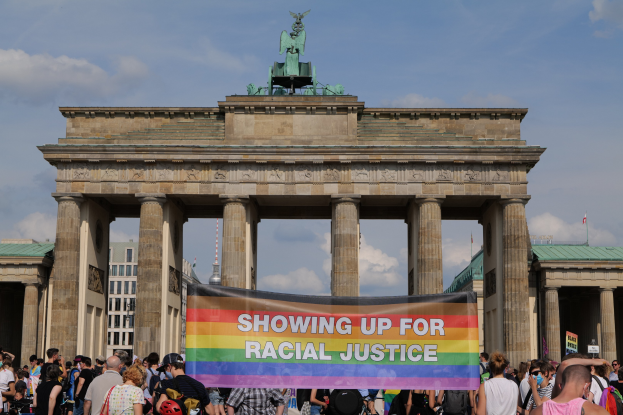 Eine Gruppe von Menschen steht vor dem Brandenburger Tor in Berlin, Deutschland, mit einer Tafel, auf der "Racial Justice" steht.