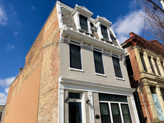 Reihe von Häusern an einer Straßenkreuzung mit Fenstern, Türen, Wandlampen, einem Baum auf der rechten Seite und einem bewölkten Himmel im Hintergrund.