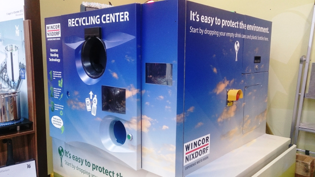 Blaues Recycling-Zentrum-Gebäude mit einem "Recycling-Zentrum"-Schild in der Mitte, einem Ständer mit verschiedenen Gegenständen links, einem einzelnen Gegenstand auf dem Boden rechts und Hintergrundbeleuchtung und Wand.