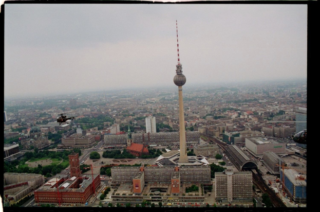 Luftaufnahme von Berlin, Deutschland, mit dem Fernsehturm in der Mitte und umgeben von Gebäuden, Bäumen, Straßen, Fahrzeugen und einem Hubschrauber.