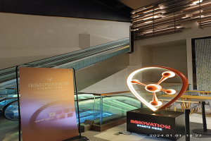 Großes Schild mit der Aufschrift "Innovation beginnt hier" vor einem Gebäude mit einer Rolltreppe, Tischen und Stühlen auf der rechten Seite und einer Tafel auf der linken Seite, die auf die HSTP20 Expo hinweist.