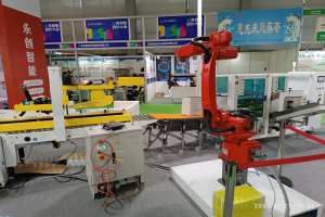 Gruppe von Robotern auf einem Tisch in einer Fabrikumgebung mit Maschinen, Kabeln, Texttafeln und Lichtern, mit Menschen im Hintergrund.