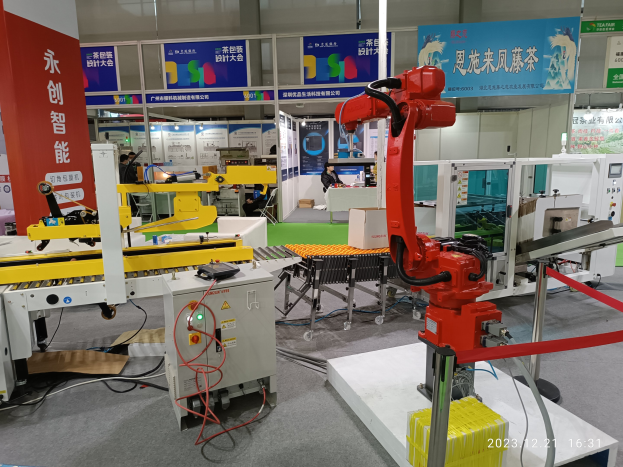 Gruppe von Robotern auf einem Tisch in einer Fabrikumgebung mit Maschinen, Kabeln, Texttafeln und Lichtern, mit Menschen im Hintergrund.